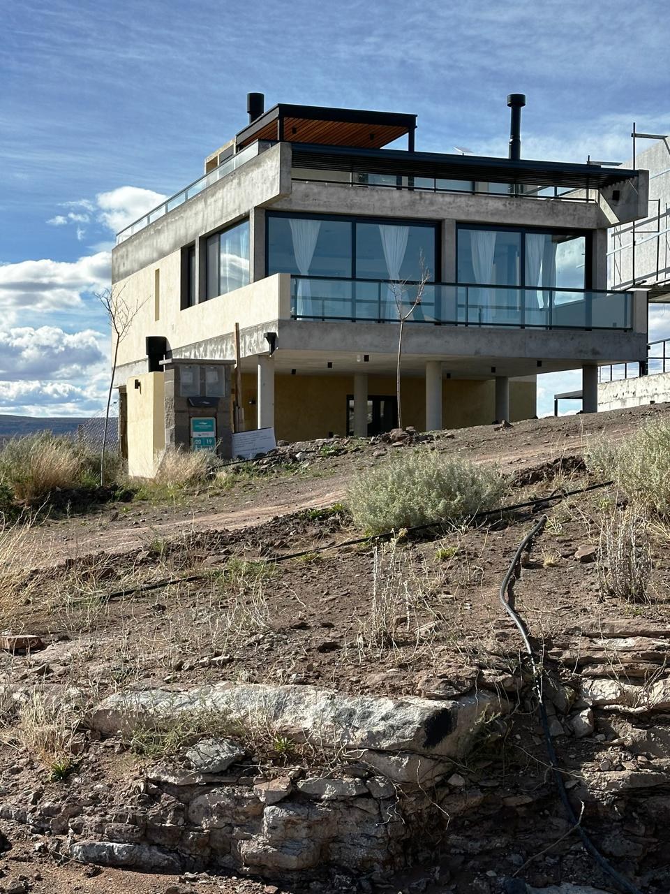 La casa sobre la ladera, con las piedras y la estepa del lote en primer plano, fotografía de obra
