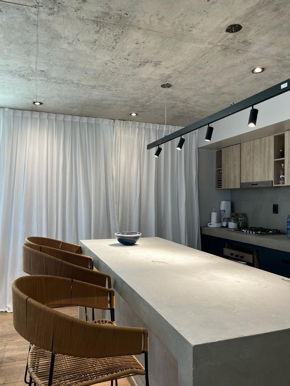 Cocina con isla de hormigón y banquetas tejidas, fotografía de obra